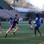 Students play flag football on a green athletic field.