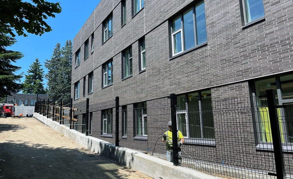 part of a 3-story brick building with a black fence behind a curb